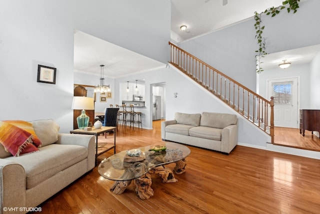 living room with crown molding, a towering ceiling, a chandelier, and light hardwood / wood-style floors