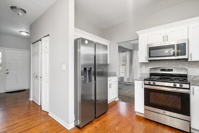 kitchen with white cabinetry, appliances with stainless steel finishes, backsplash, and light hardwood / wood-style flooring