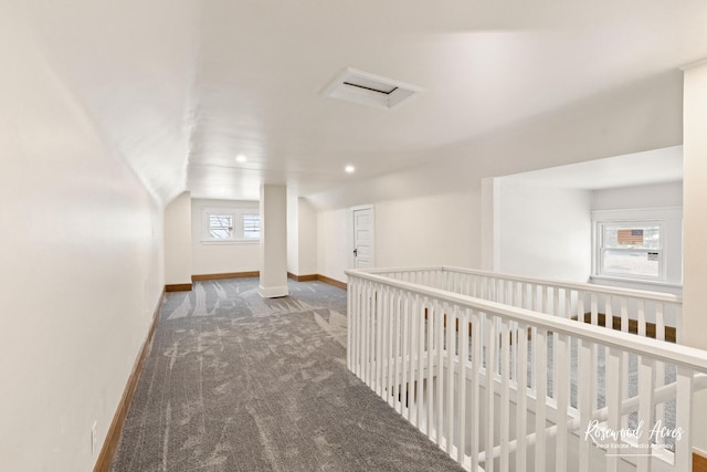 hall featuring lofted ceiling and dark colored carpet