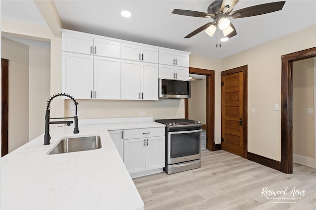 kitchen featuring appliances with stainless steel finishes, sink, light wood-type flooring, white cabinetry, and ceiling fan