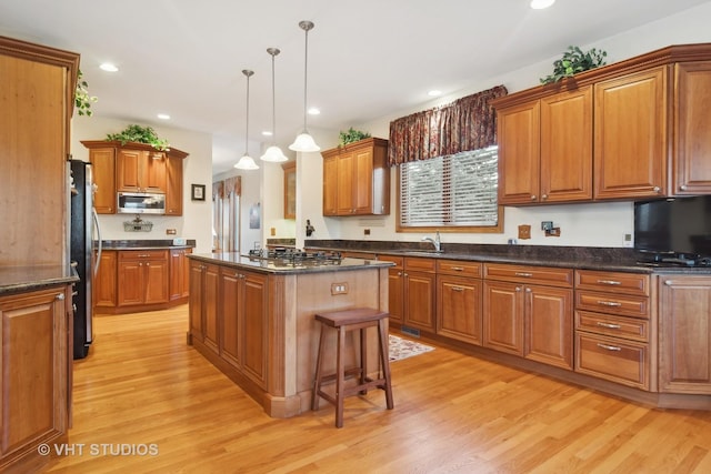 kitchen featuring sink, appliances with stainless steel finishes, hanging light fixtures, a center island, and light wood-type flooring