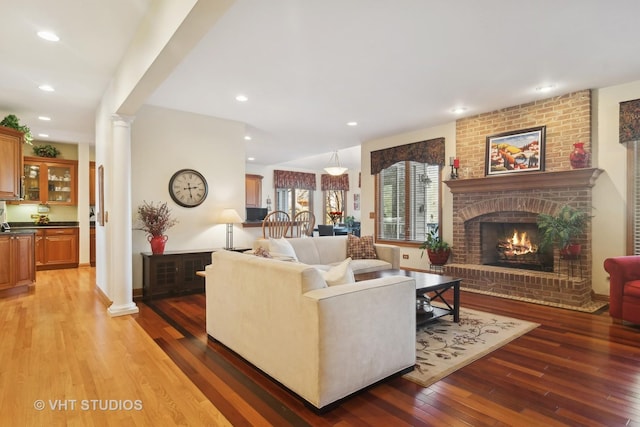 living room with a brick fireplace, hardwood / wood-style flooring, and ornate columns