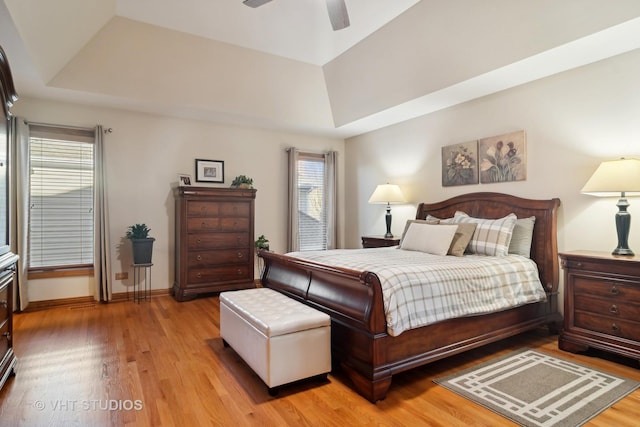 bedroom featuring ceiling fan, lofted ceiling, a tray ceiling, and light hardwood / wood-style flooring