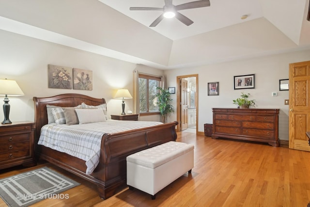 bedroom featuring a tray ceiling, ensuite bath, ceiling fan, and light wood-type flooring