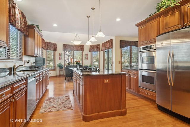 kitchen with sink, light hardwood / wood-style flooring, a kitchen island, pendant lighting, and stainless steel appliances