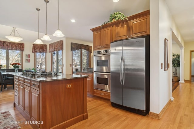 kitchen featuring appliances with stainless steel finishes, dark stone countertops, hanging light fixtures, a kitchen island, and light wood-type flooring