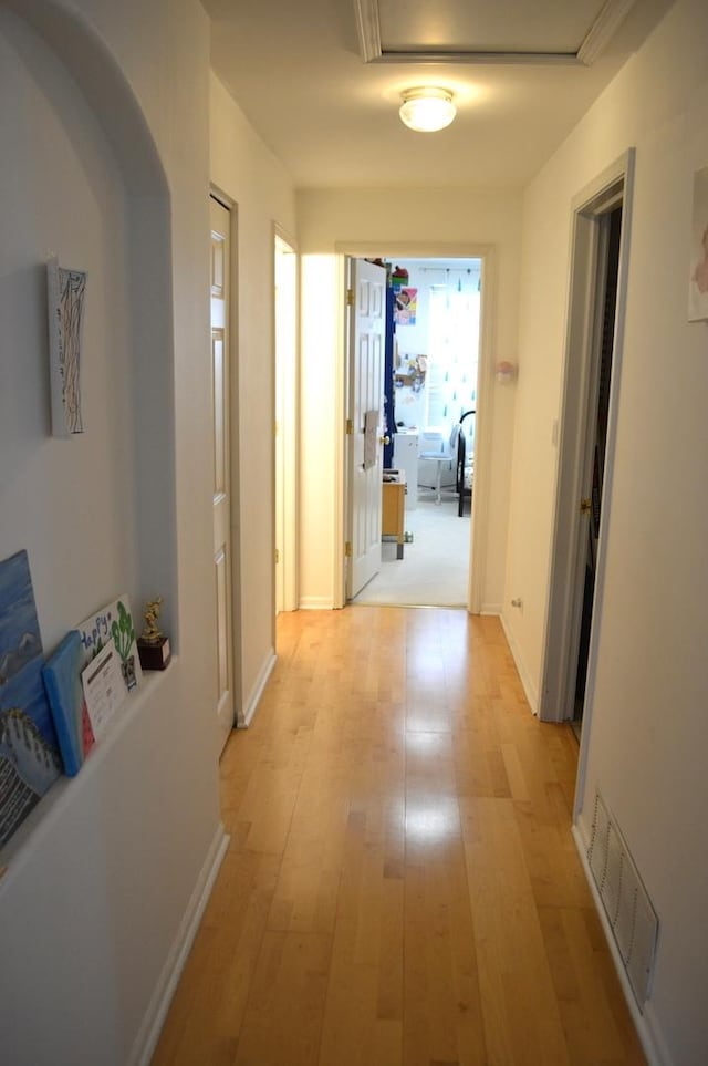 hallway with light wood-style floors, visible vents, and baseboards