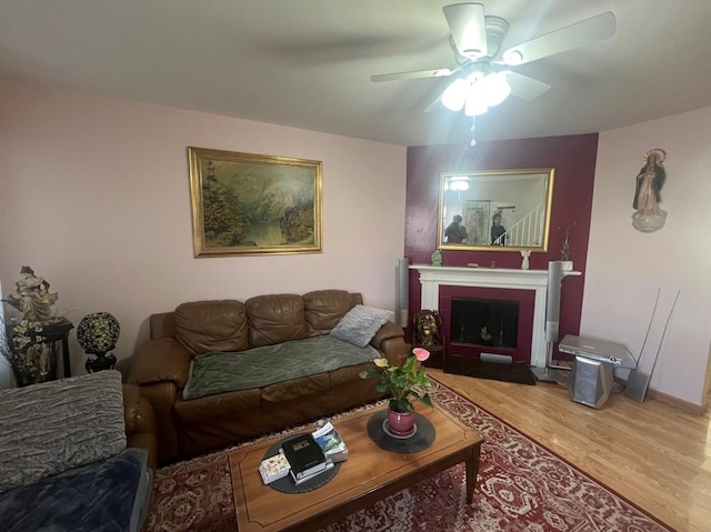 living room featuring a fireplace with flush hearth, ceiling fan, and wood finished floors