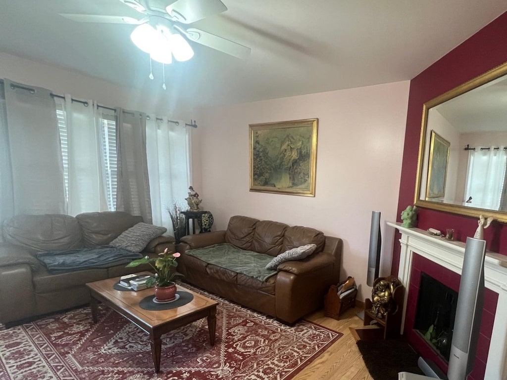 living area featuring a fireplace with flush hearth, ceiling fan, and wood finished floors