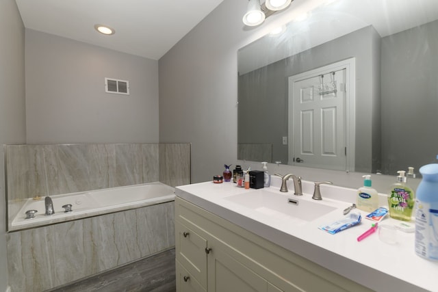 bathroom featuring a relaxing tiled tub, vanity, and wood-type flooring