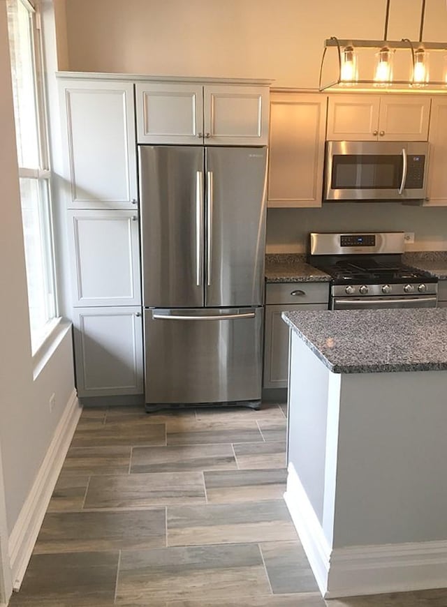 kitchen with hanging light fixtures, stainless steel appliances, dark stone counters, and a healthy amount of sunlight