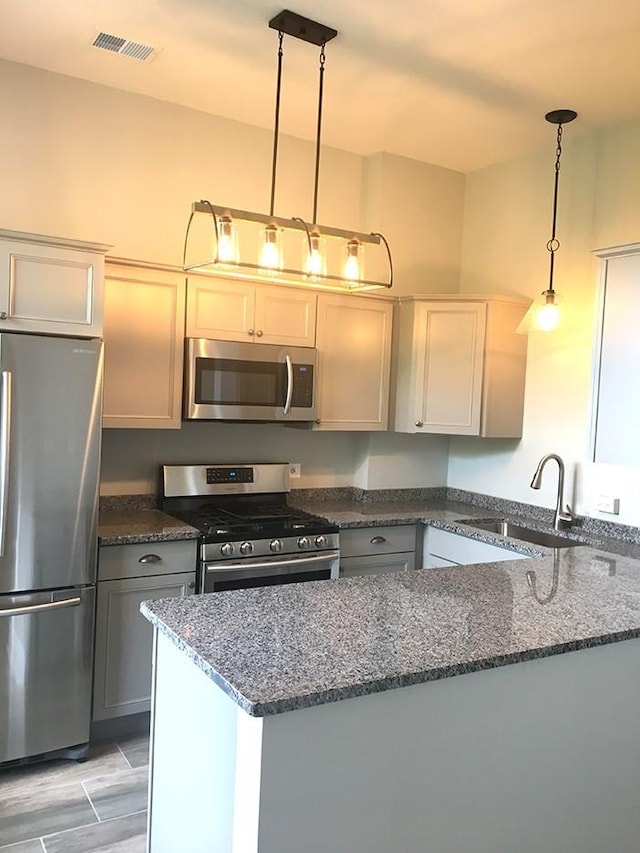 kitchen featuring sink, gray cabinetry, dark stone countertops, pendant lighting, and stainless steel appliances