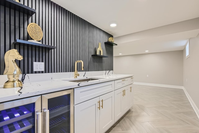 bar featuring sink, light stone counters, light parquet flooring, beverage cooler, and white cabinets