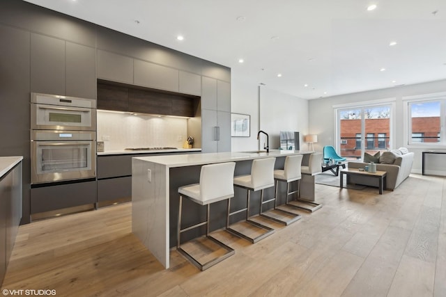 kitchen featuring a kitchen bar, gray cabinets, light hardwood / wood-style floors, and an island with sink