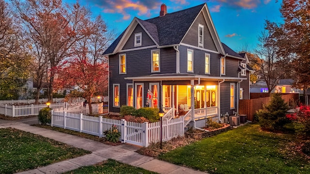 back house at dusk featuring cooling unit, a lawn, and a porch