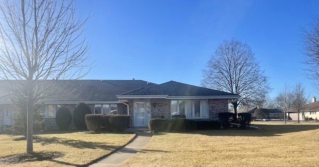 view of front of home with a shingled roof, a front yard, and brick siding