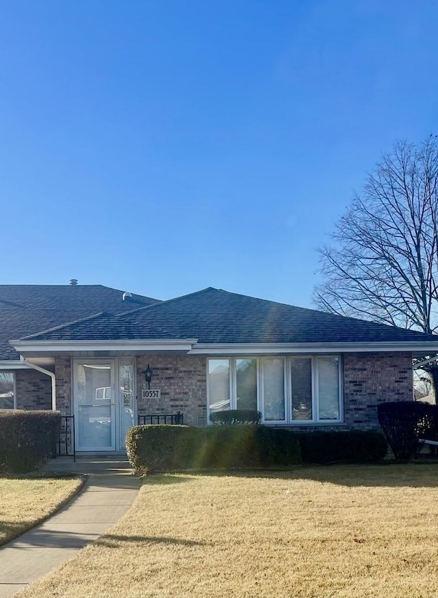 ranch-style house featuring roof with shingles, brick siding, and a front lawn