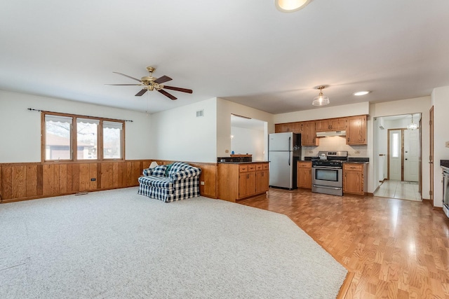 interior space featuring wooden walls, a wainscoted wall, ceiling fan, brown cabinets, and stainless steel appliances