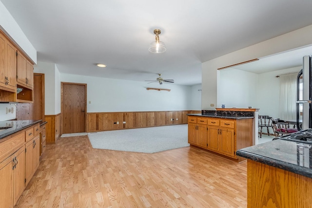 kitchen featuring brown cabinetry, dark stone counters, wainscoting, and light wood finished floors