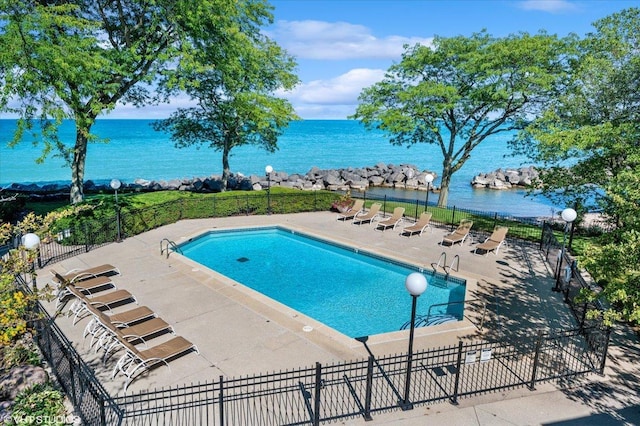 community pool with a patio, a water view, and fence