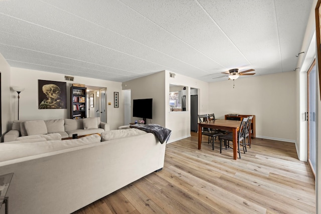 living room with light wood-type flooring, ceiling fan, and a textured ceiling