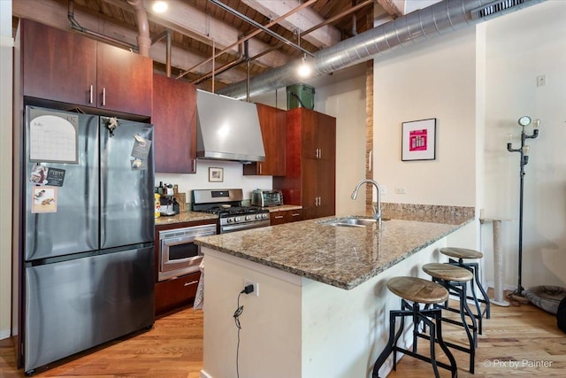 kitchen with wall chimney exhaust hood, a kitchen bar, sink, appliances with stainless steel finishes, and stone counters