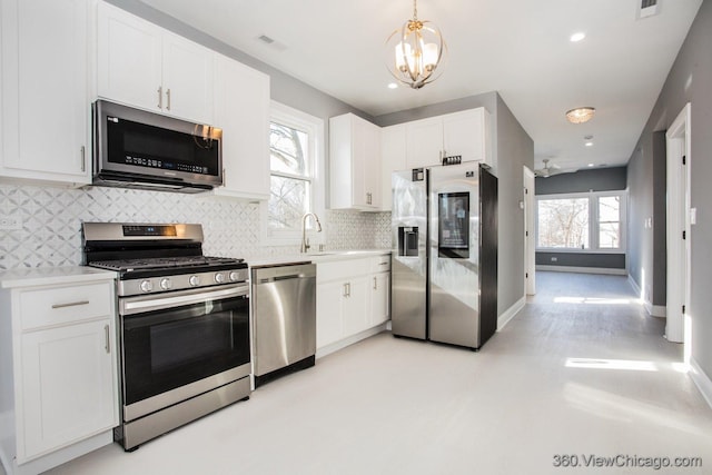 kitchen featuring sink, appliances with stainless steel finishes, white cabinetry, decorative backsplash, and decorative light fixtures