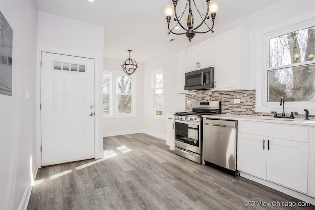 kitchen featuring appliances with stainless steel finishes, pendant lighting, white cabinets, a chandelier, and backsplash