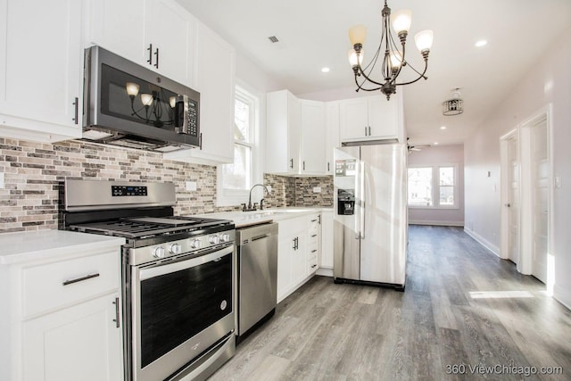 kitchen featuring appliances with stainless steel finishes, pendant lighting, white cabinets, backsplash, and light wood-type flooring