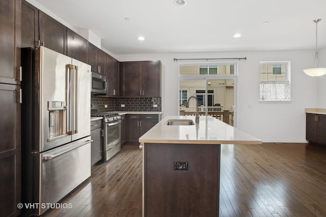 kitchen with sink, appliances with stainless steel finishes, dark brown cabinets, an island with sink, and decorative light fixtures