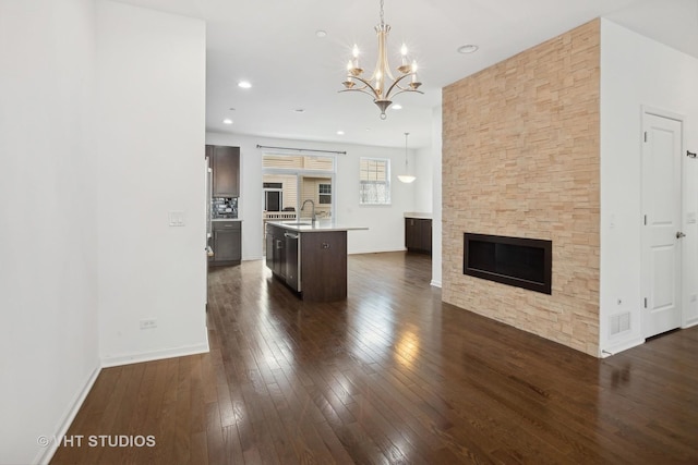 kitchen with hanging light fixtures, an island with sink, sink, and dark hardwood / wood-style floors