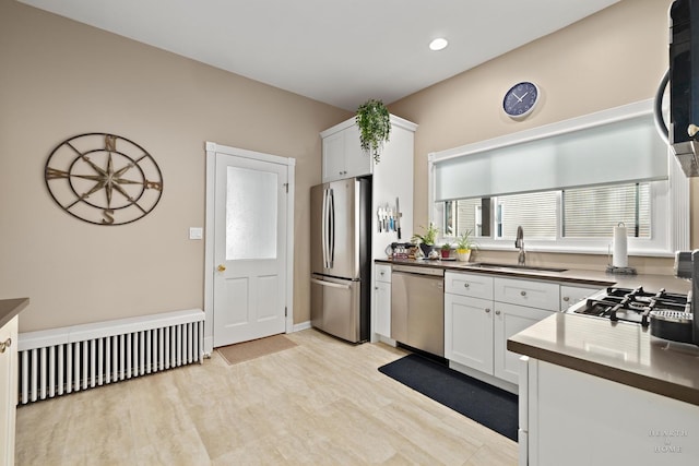 kitchen with sink, light wood-type flooring, white cabinets, and appliances with stainless steel finishes