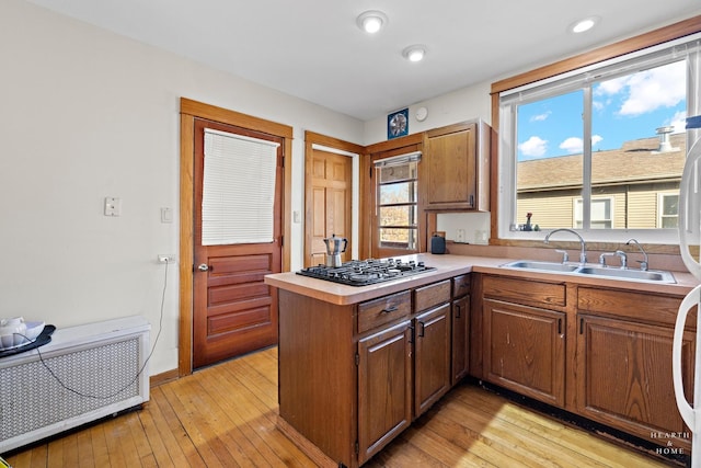 kitchen with stainless steel gas cooktop, sink, light wood-type flooring, radiator, and kitchen peninsula