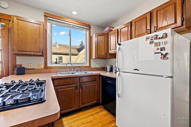 kitchen with dishwasher, stovetop, sink, white fridge, and light hardwood / wood-style floors