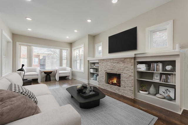 living room featuring hardwood / wood-style floors, built in shelves, and a stone fireplace