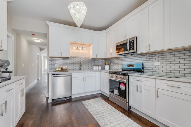 kitchen with appliances with stainless steel finishes, white cabinets, dark hardwood / wood-style flooring, and pendant lighting