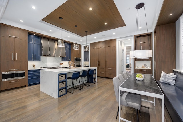 kitchen with light countertops, wall chimney range hood, a kitchen bar, modern cabinets, and a raised ceiling