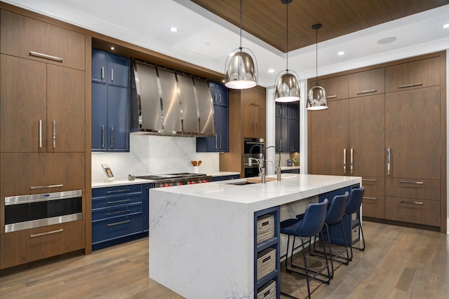 kitchen featuring light wood-style flooring, a kitchen breakfast bar, wall chimney range hood, decorative backsplash, and a raised ceiling