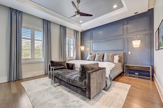 bedroom featuring a tray ceiling, light wood-type flooring, and a decorative wall