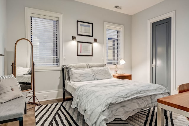 bedroom featuring multiple windows, visible vents, baseboards, and wood finished floors