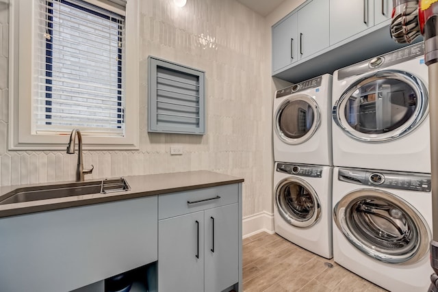 washroom with independent washer and dryer, cabinet space, a sink, and stacked washing maching and dryer