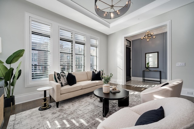 living room with baseboards, a raised ceiling, wood finished floors, and an inviting chandelier