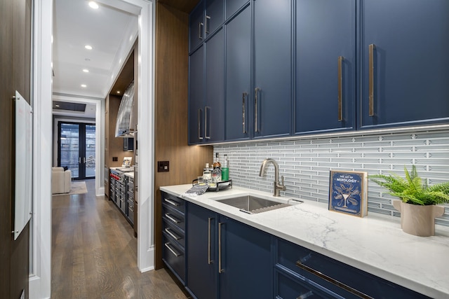 kitchen featuring decorative backsplash, dark wood-type flooring, light stone countertops, blue cabinetry, and a sink