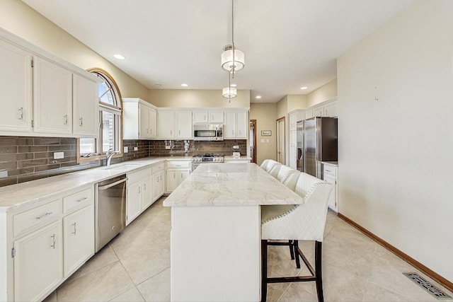 kitchen with appliances with stainless steel finishes, white cabinets, decorative backsplash, a kitchen island, and a kitchen bar