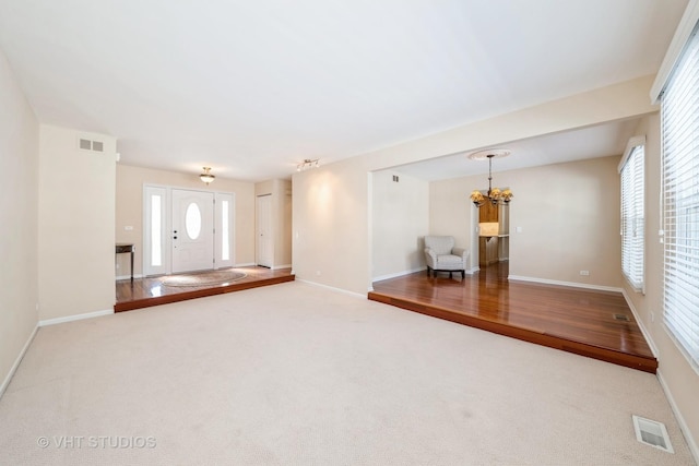 unfurnished living room with carpet floors, visible vents, a notable chandelier, and baseboards