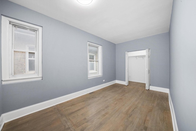 unfurnished bedroom with a closet, wood finished floors, visible vents, and baseboards