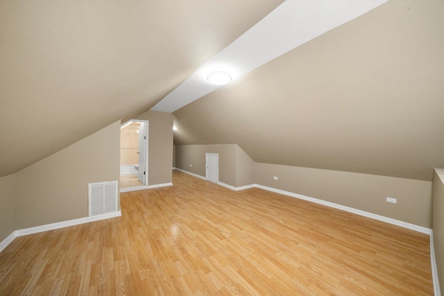 additional living space featuring vaulted ceiling, light wood finished floors, visible vents, and baseboards