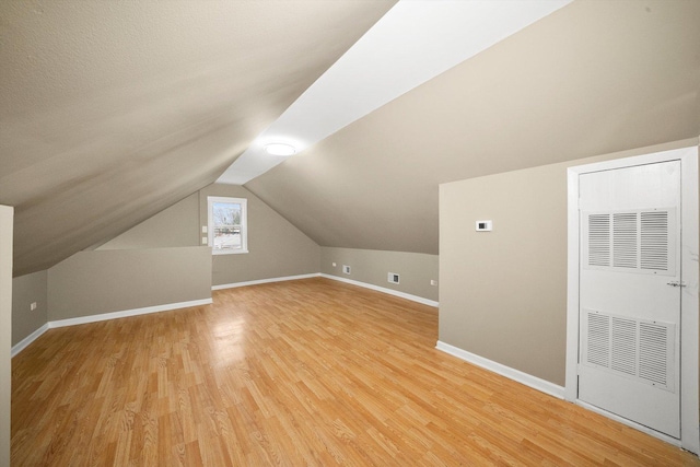 additional living space with lofted ceiling, a heating unit, light wood-style flooring, and baseboards