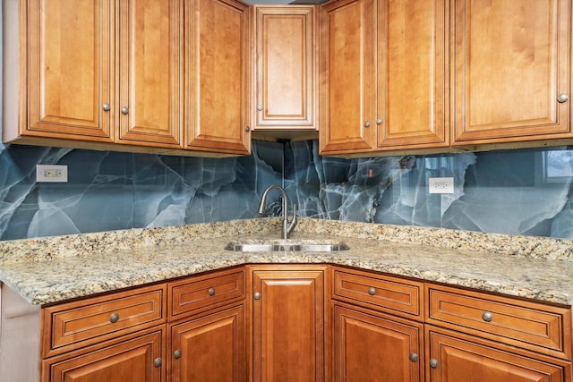 kitchen featuring backsplash, a sink, light stone countertops, and brown cabinets