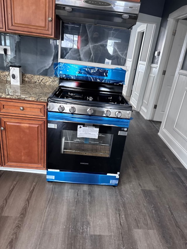 interior space featuring stone countertops, brown cabinetry, dark wood finished floors, range hood, and stainless steel stove